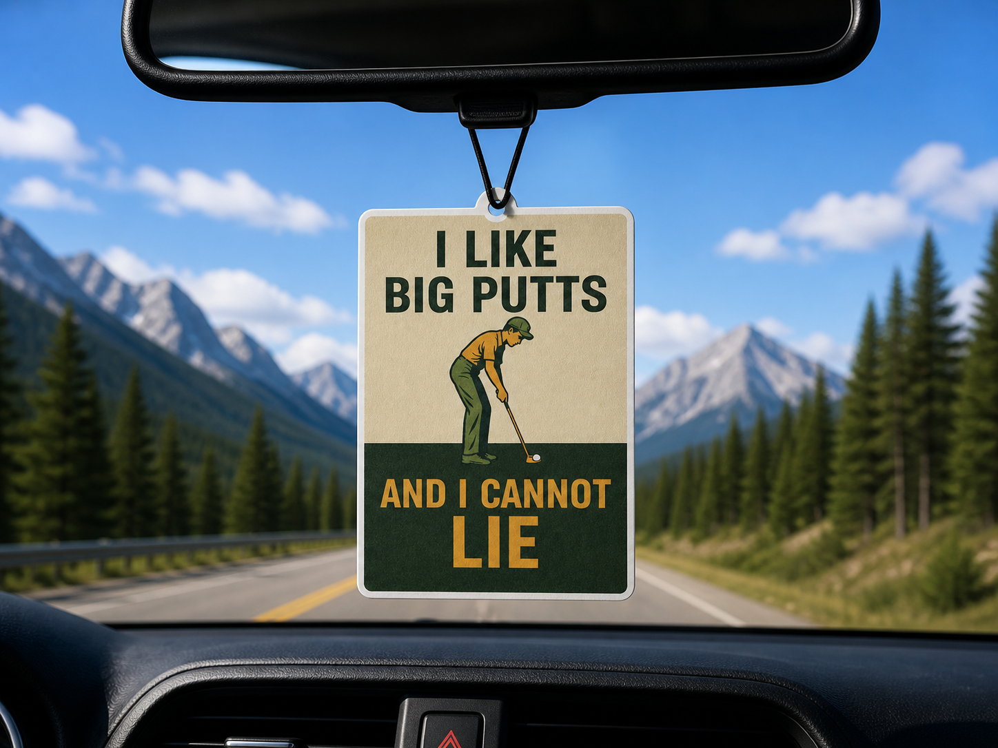 Car air freshener with a humorous golf-themed message hanging from a car's rearview mirror with a scenic road and mountains in the background.
