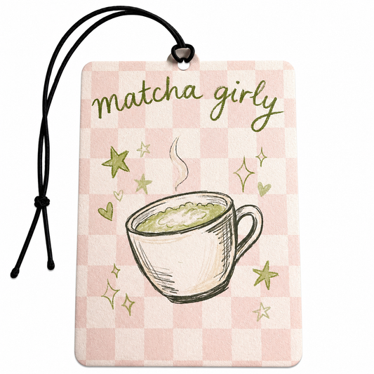 A rectangular car air freshener with a black hanging cord, featuring a pink and white checkerboard pattern, the phrase 'matcha girly' in green script, and an illustration of a matcha cup with green stars and hearts.