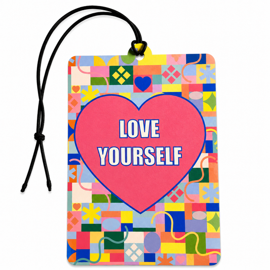 A rectangular car air freshener or tag with a black hanging cord, featuring a colorful mosaic background and a large pink heart in the center with the words 'LOVE YOURSELF' in white text.