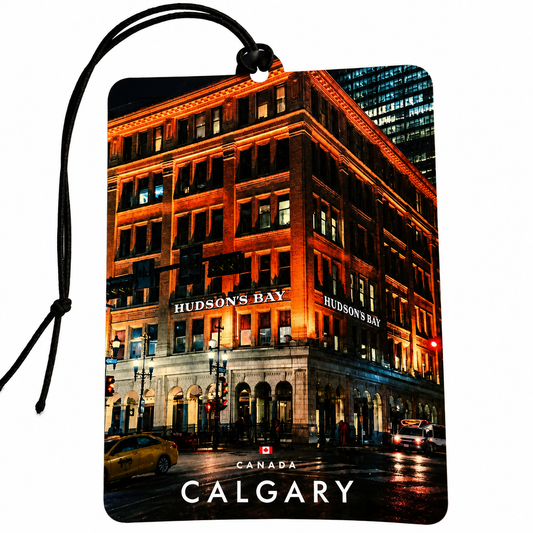 A rectangular car air freshener or luggage tag with a black hanging cord, printed with a nighttime city photograph of Hudson's Bay in Calgary, Canada. The print shows a warmly lit brick building, street, and the words 'HUDSON'S BAY' and 'CALGARY' at the bottom.
