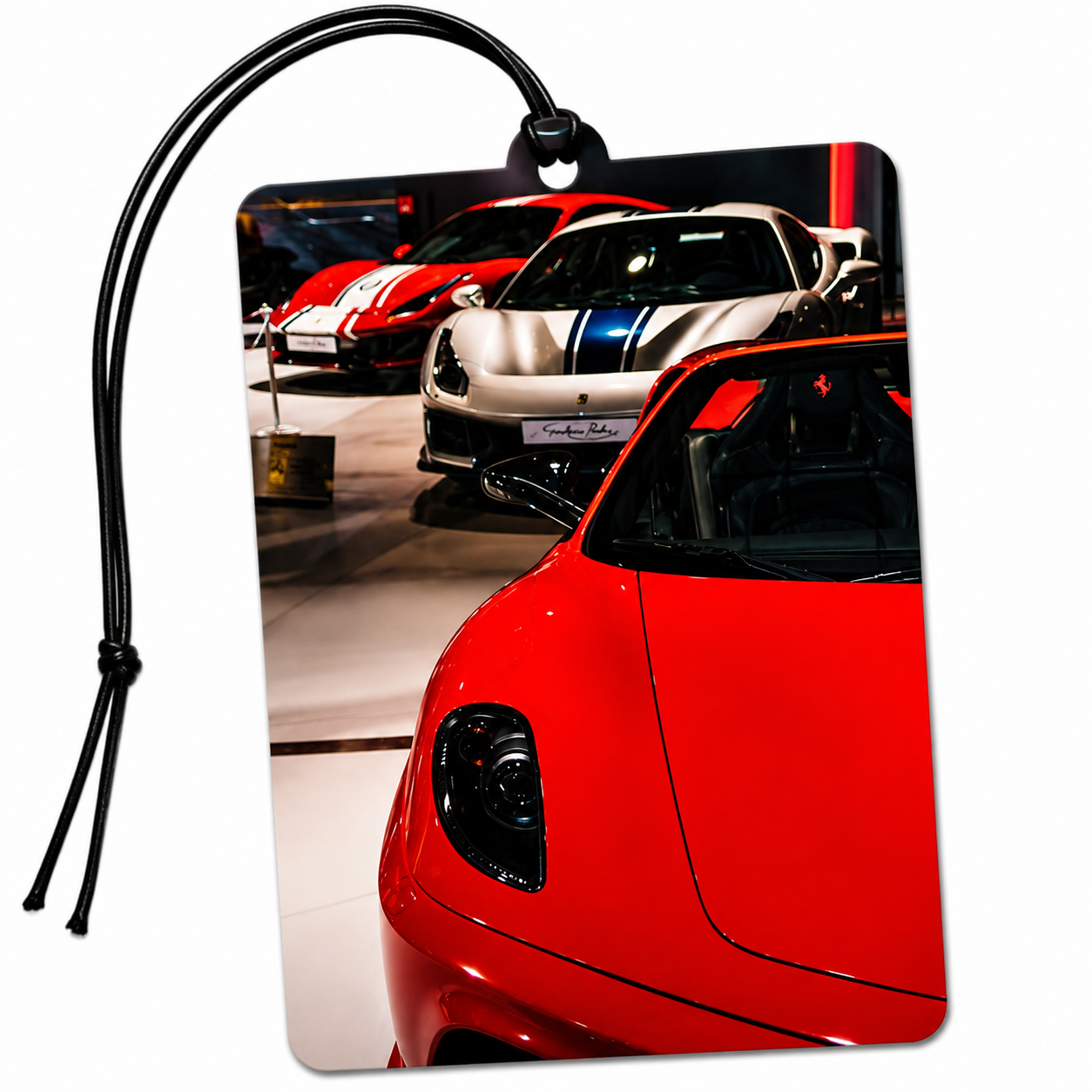 A rectangular car-shaped car air freshener featuring a printed photograph of sports cars in a showroom, complete with a black hanging loop and string, shown on a plain white background.