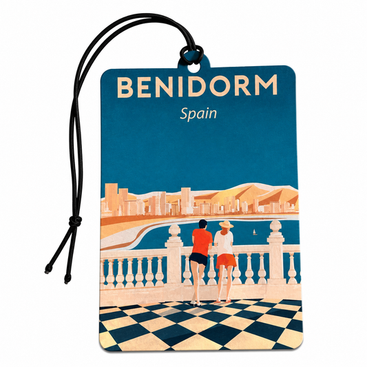A Benidorm Spain travel luggage tag featuring a retro-style travel poster illustration. The tag has a dark blue background with the text 'BENIDORM Spain' in cream and white, and an illustration of two people standing on a checkered balcony overlooking a coastal city and sea.