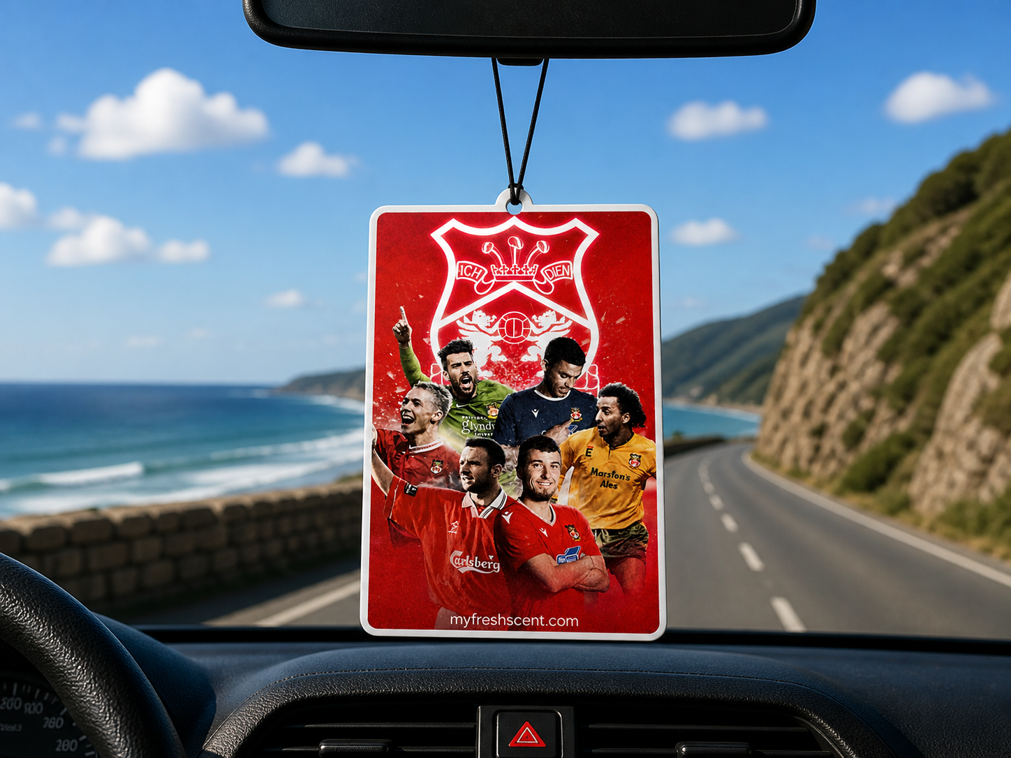 Car air freshener with ledgenary wrexham afc players on a dashboard with a scenic road and ocean view.
