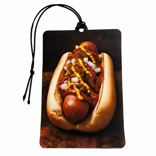A rectangular car air freshener or magnet with rounded corners, featuring a printed photograph of a hot dog topped with mustard, ketchup, onions, and relish. The item has a black hanging string and is shown against a plain white background.