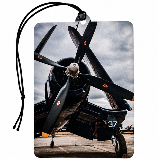 A rectangular luggage tag or car air freshener with rounded corners featuring a printed photograph of a black vintage propeller airplane on a cloudy sky background. The tag has a black hanging cord and a small metal grommet at the top.